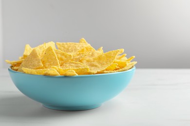 Photo of Tortilla chips (nachos) in bowl on white table against grey background, closeup