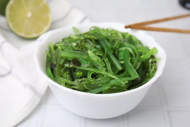 Photo of Tasty seaweed salad in bowl served on white tiled table, closeup