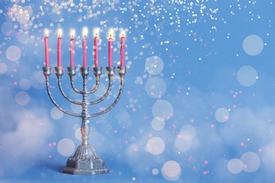 Image of Silver menorah with burning candles on blue background, space for text. Hanukkah celebration