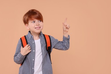Photo of Happy schoolboy with backpack pointing at something on beige background. Space for text