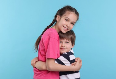 Happy brother and sister hugging on light blue background