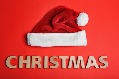 Santa Claus red hat and word Christmas made of wooden letters on color background, top view