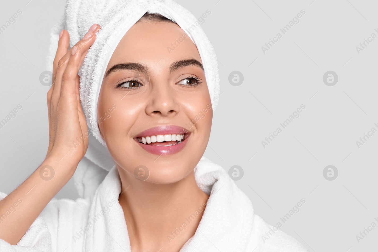 Photo of Young woman in bathrobe with towel on light grey background, space for text. Spa treatment