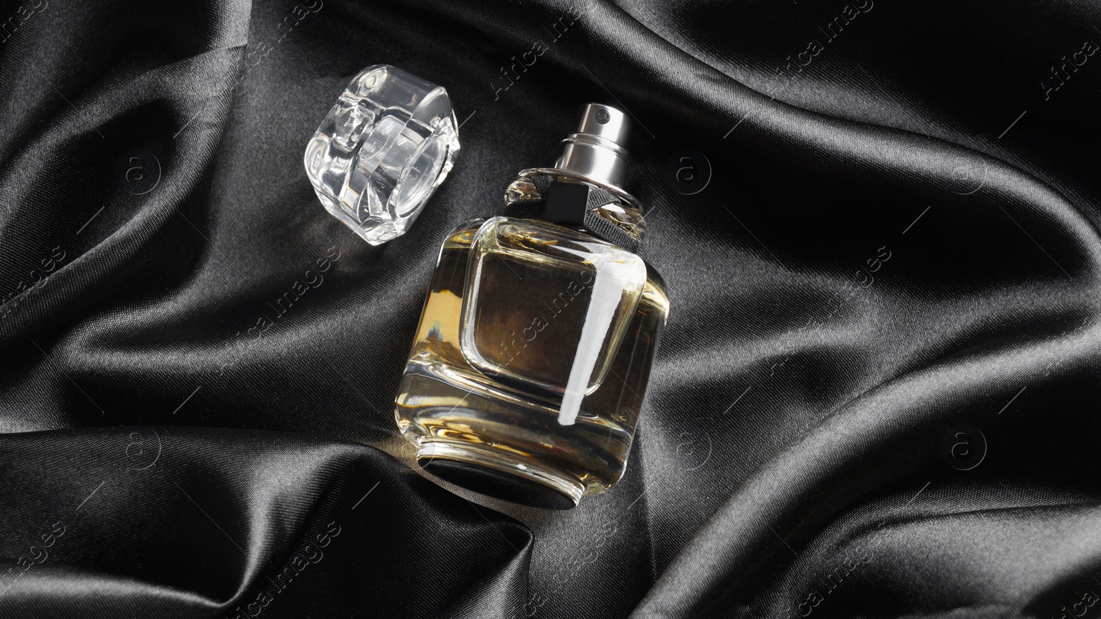 Photo of Luxury bottle of perfume on black silk, top view