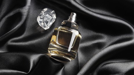 Luxury bottle of perfume on black silk, top view