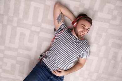 Photo of Young man in headphones enjoying music on floor, top view