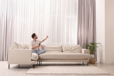 Photo of Man using smartphone on sofa near window with beautiful curtains in living room