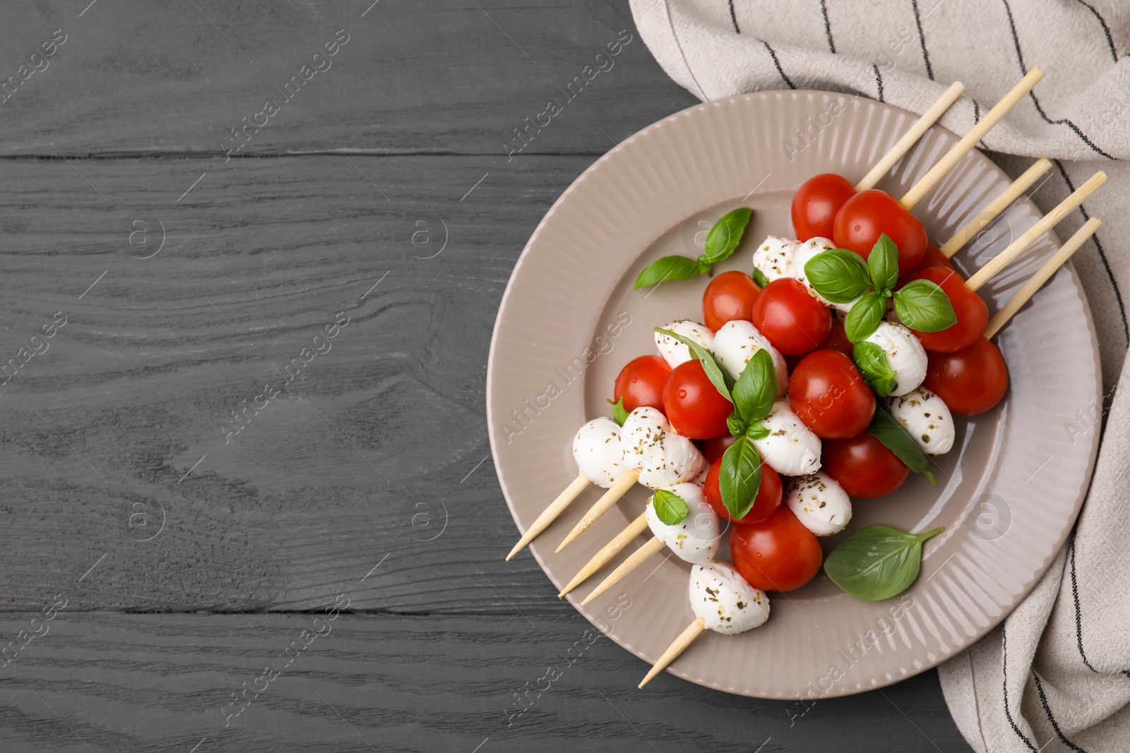 Photo of Caprese skewers with tomatoes, mozzarella balls, basil and spices on grey wooden table, top view. Space for text