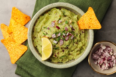 Photo of Bowl of delicious guacamole, nachos chips and lime on grey table, flat lay