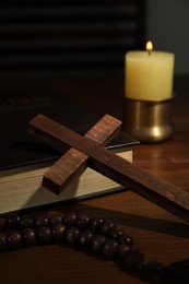 Photo of Cross, rosary beads, Bible and church candle on wooden table