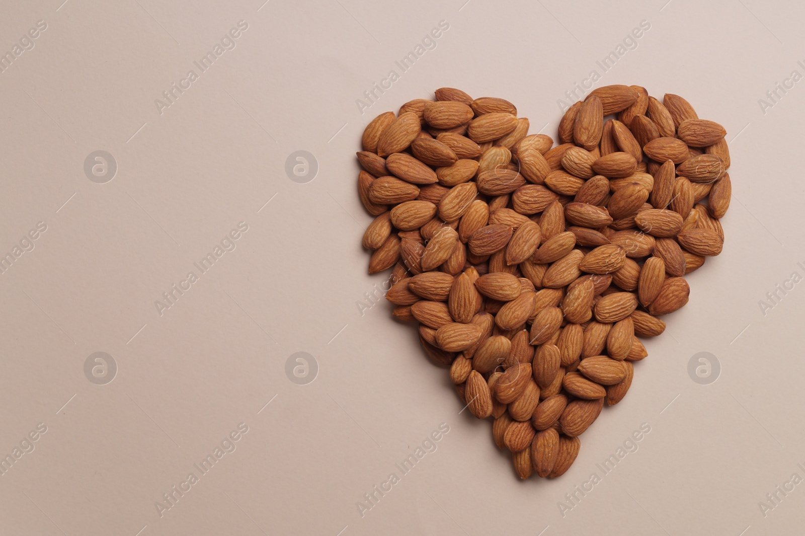 Photo of Heart made of delicious raw almonds on beige background, flat lay. Space for text