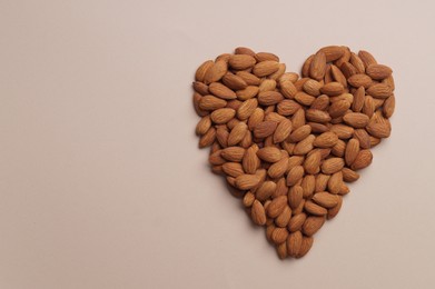 Heart made of delicious raw almonds on beige background, flat lay. Space for text