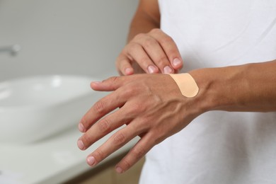 Photo of Man putting sticking plaster onto hand indoors, closeup