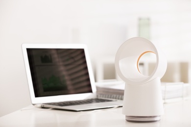 Photo of Modern electric fan and laptop on table in office