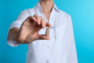 Female doctor holding hearing aid on color background, closeup. Medical object