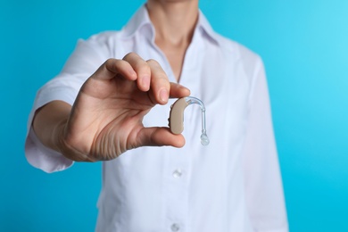 Photo of Female doctor holding hearing aid on color background, closeup. Medical object