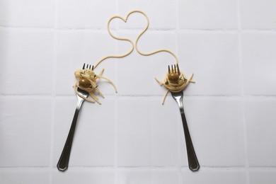 Photo of Heart made of tasty spaghetti, forks and olives on white tiled table, top view