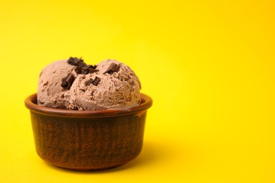 Photo of Bowl of tasty ice cream with chocolate chunks on yellow background, closeup. Space for text