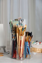 Photo of Glass jars with many different paintbrushes on white wooden table indoors