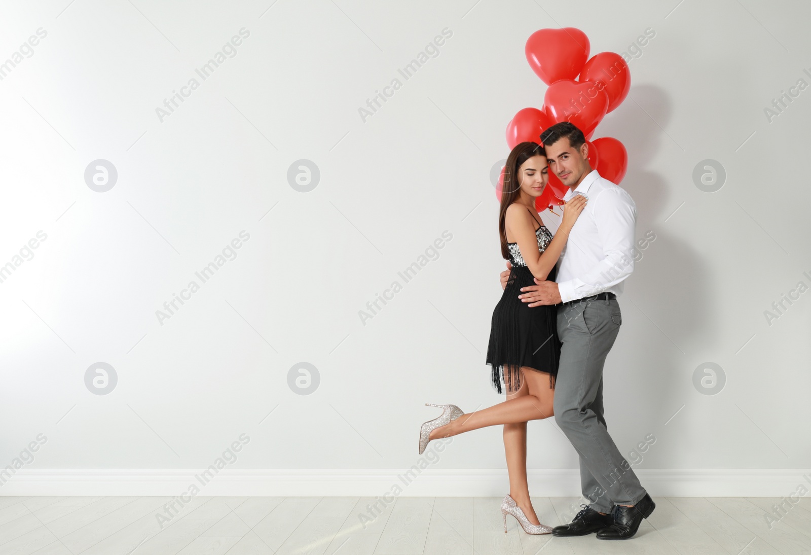 Photo of Beautiful couple with heart shaped balloons near light wall, space for text