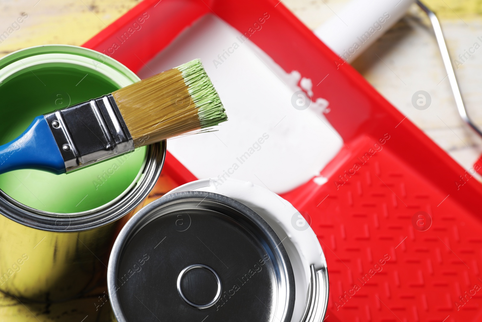 Photo of Cans of paints, brush and tray on table, closeup