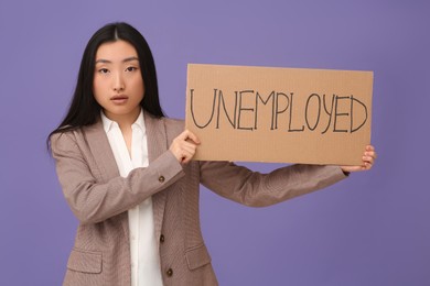 Photo of Asian woman holding sign with word Unemployed on purple background