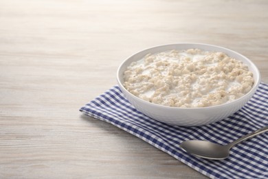 Photo of Tasty boiled oatmeal in bowl and spoon on wooden table. Space for text