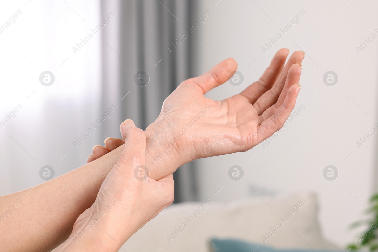 Photo of Woman suffering from pain in wrist indoors, closeup. Arthritis symptoms