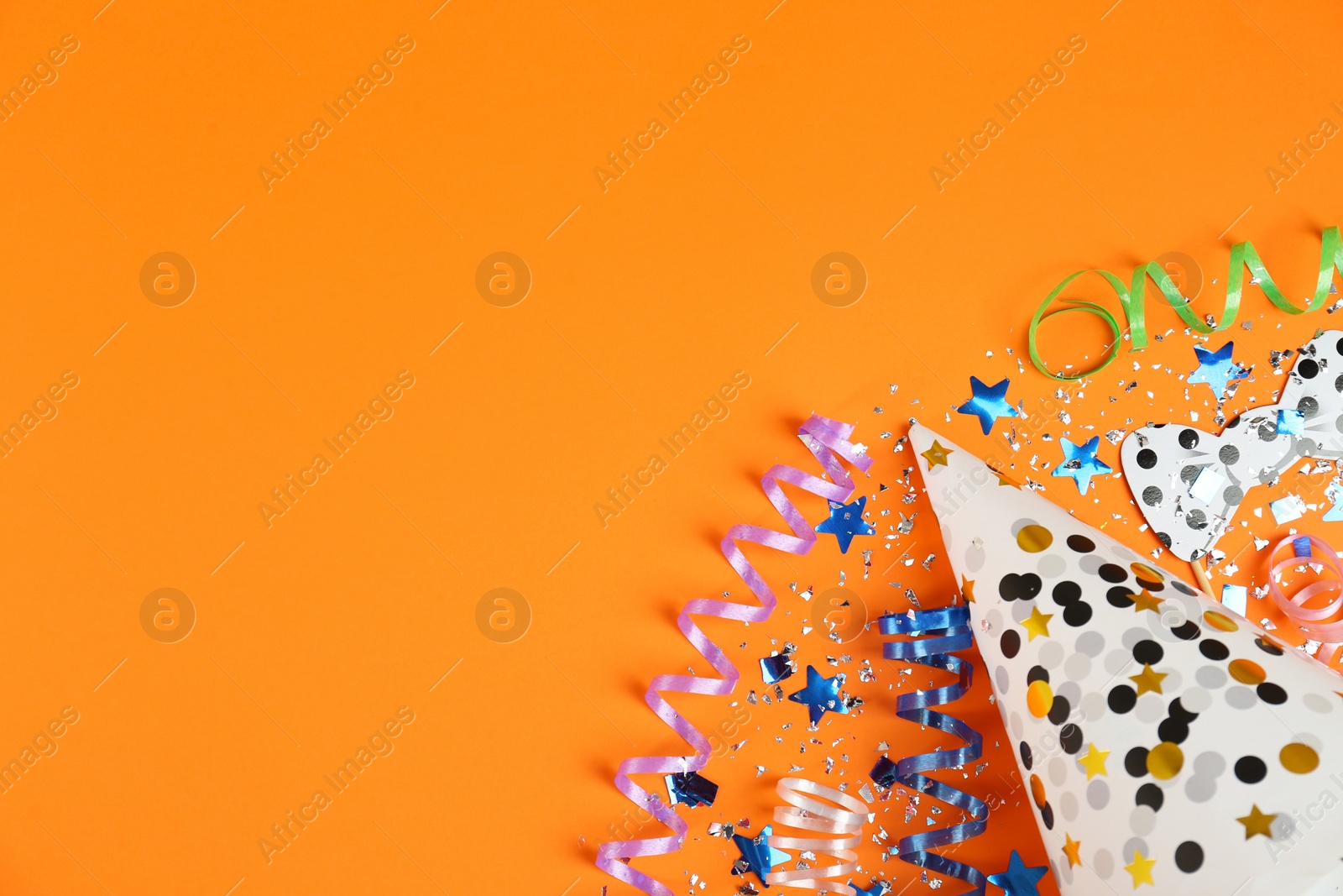 Photo of Colorful serpentine streamers, confetti and cap on orange background, flat lay. Space for text