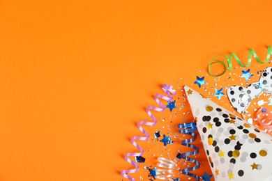 Photo of Colorful serpentine streamers, confetti and cap on orange background, flat lay. Space for text