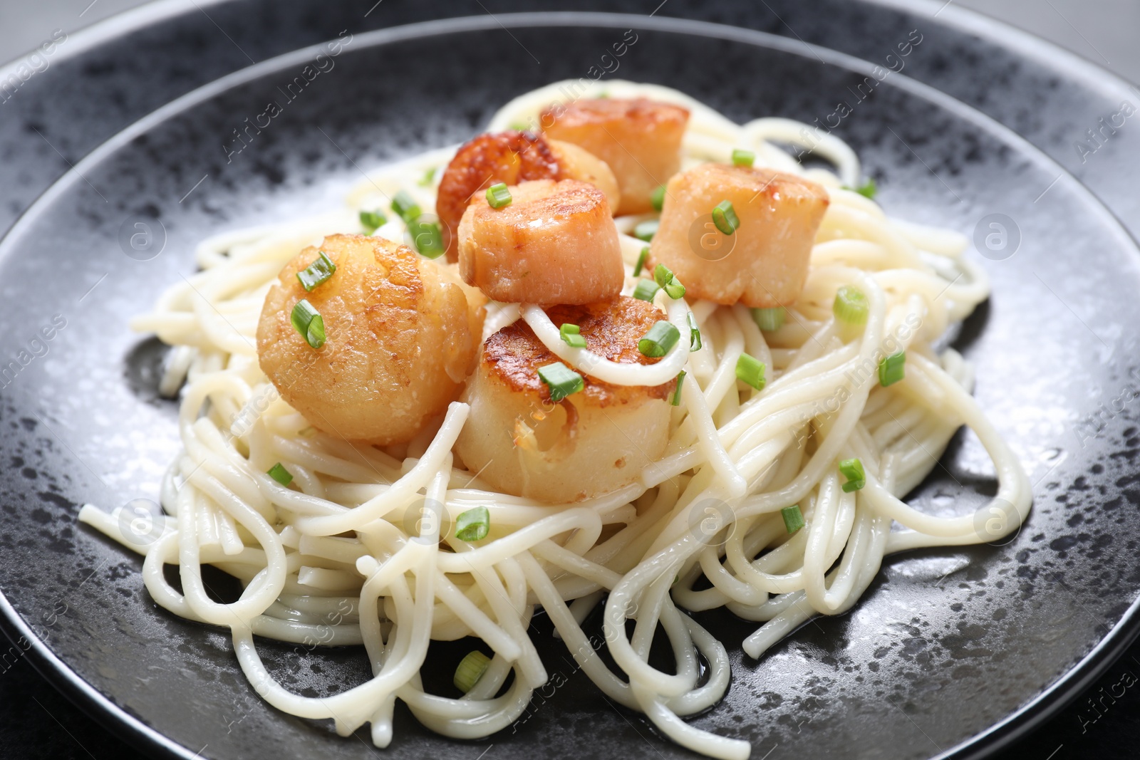 Photo of Delicious scallop pasta with green onion on plate, closeup