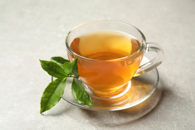 Photo of Cup of green tea and leaves on grey table