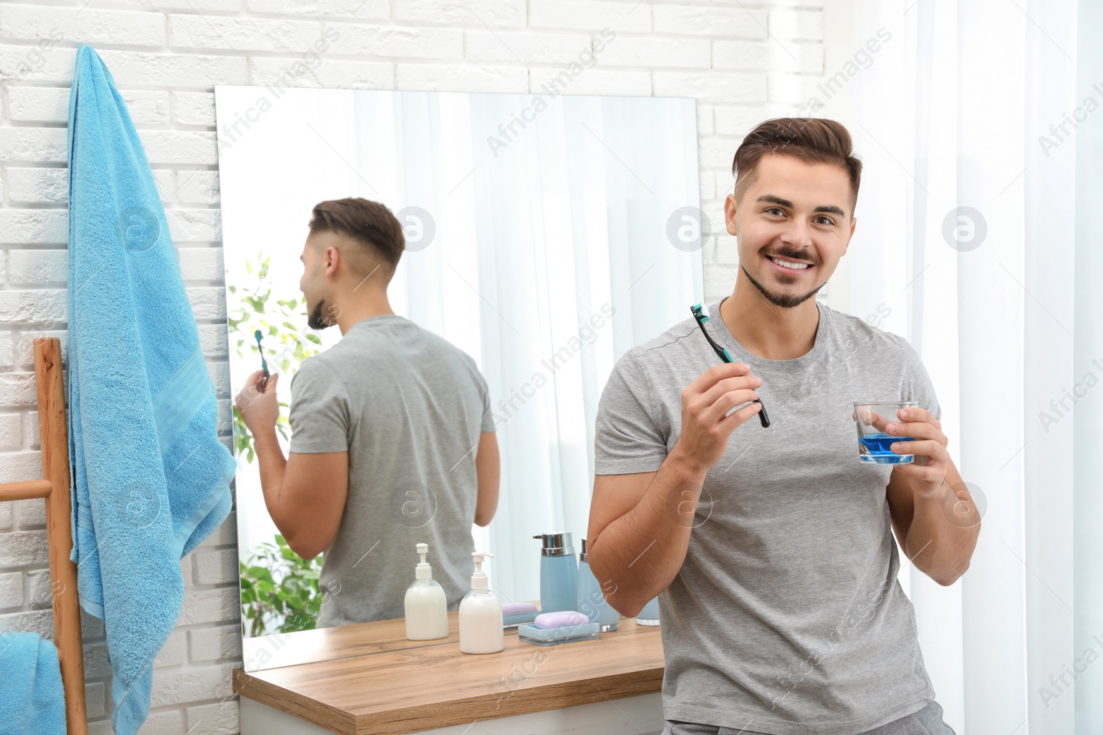 Photo of Young man with toothbrush and glass of mouthwash in bathroom at home, space for text. Teeth and oral care