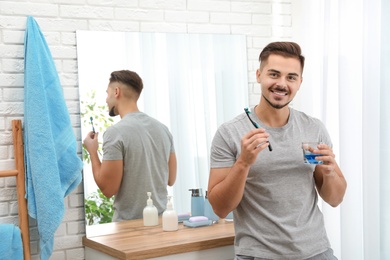 Photo of Young man with toothbrush and glass of mouthwash in bathroom at home, space for text. Teeth and oral care
