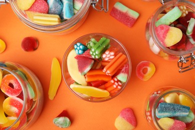 Tasty jelly candies in jars on orange background, flat lay