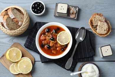 Photo of Meat solyanka soup with sausages, olives and vegetables served on grey wooden table, flat lay