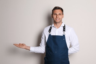 Photo of Portrait of happy young waiter in uniform on light background