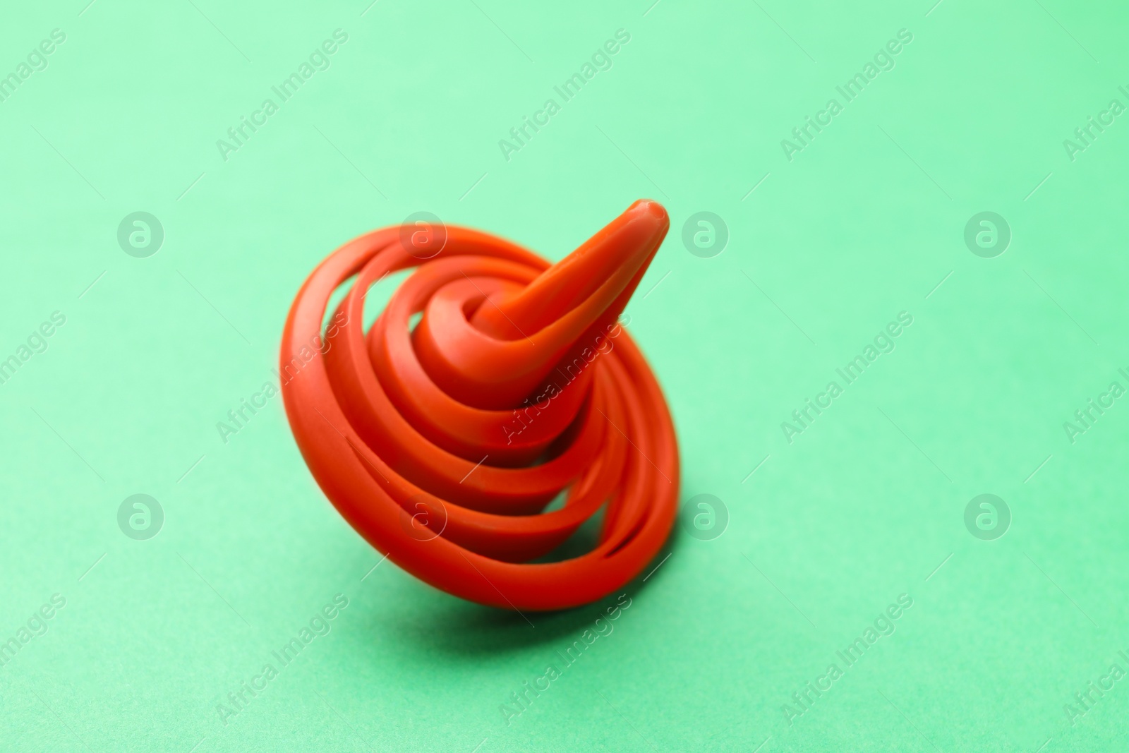 Photo of One orange spinning top on green background, closeup. Space for text