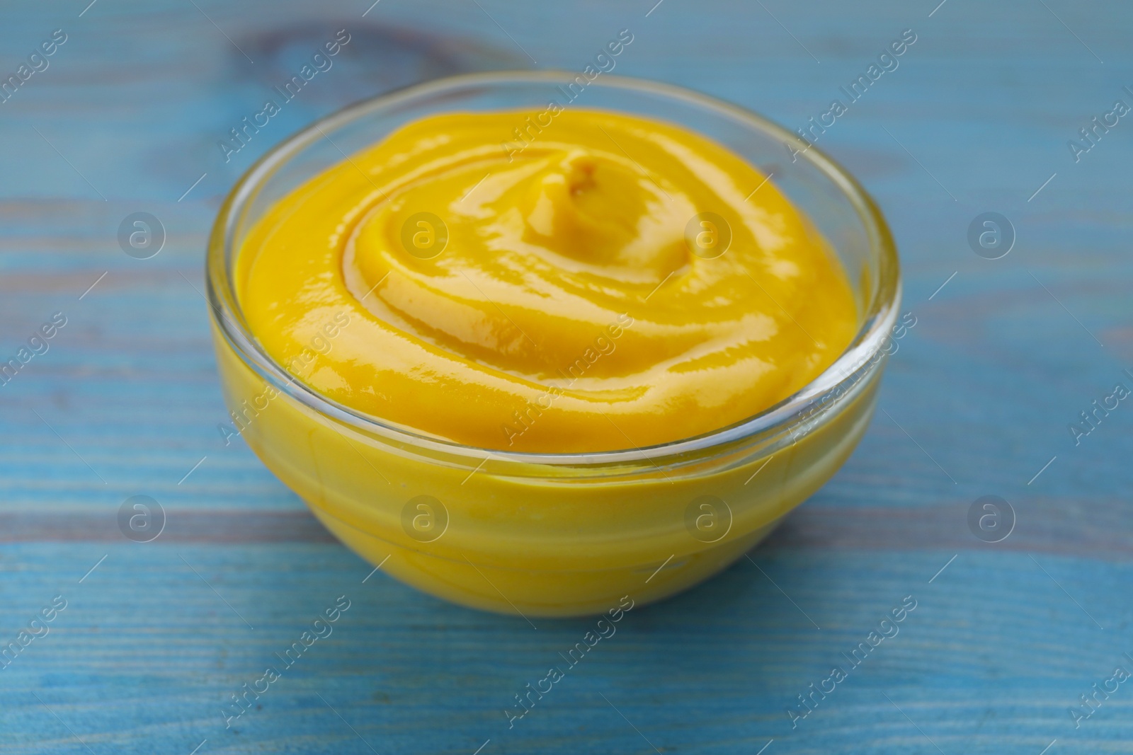 Photo of Sauce bowl with delicious mustard on light blue wooden table, closeup