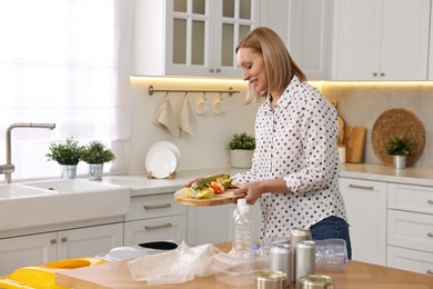 Smiling woman separating garbage at table in kitchen