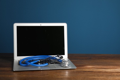 Photo of Modern laptop with stethoscope on table against color wall. Mockup for design