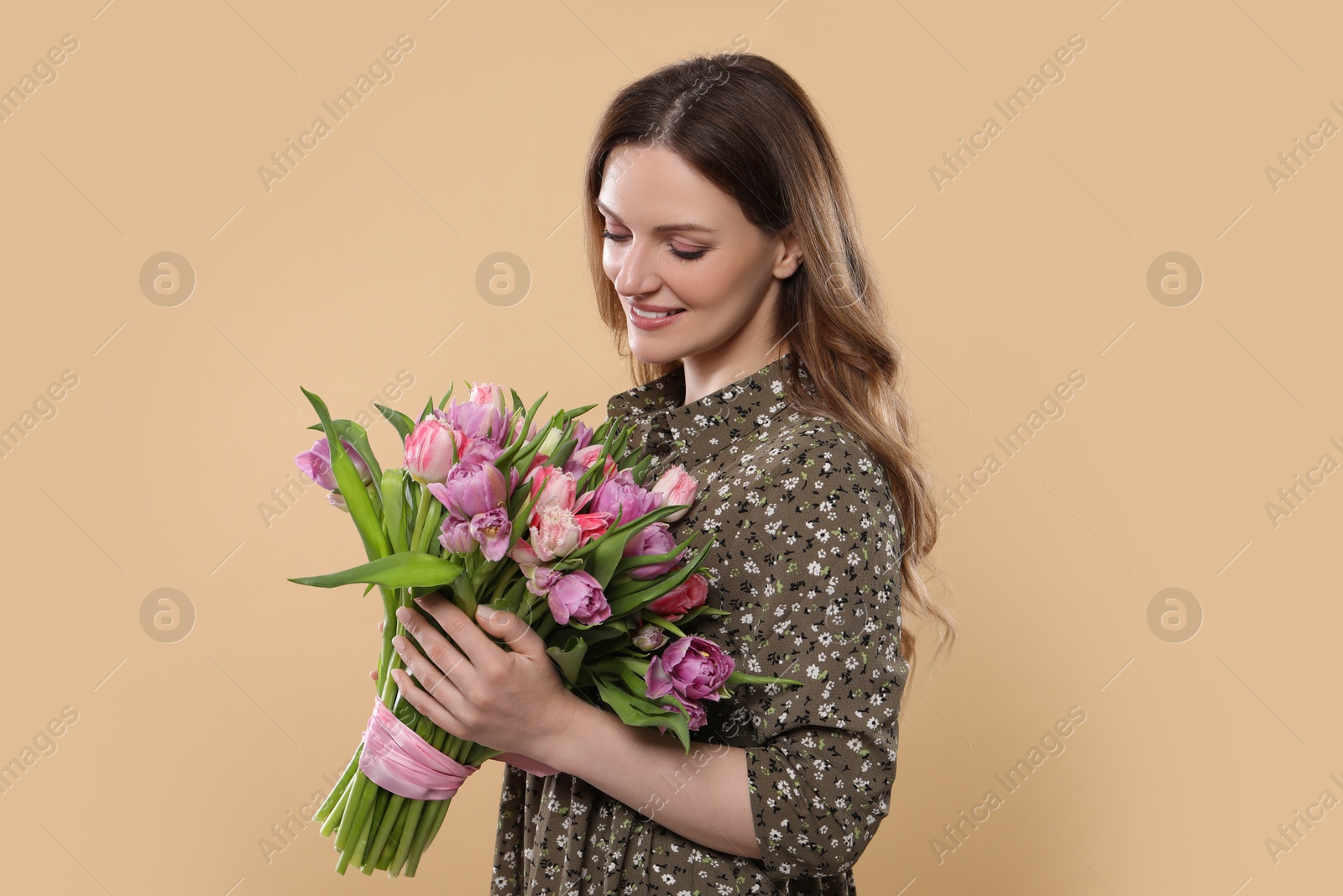 Photo of Happy young woman holding bouquet of beautiful tulips on beige background