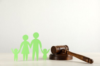 Paper family figure and wooden gavel on white table. Child adoption concept