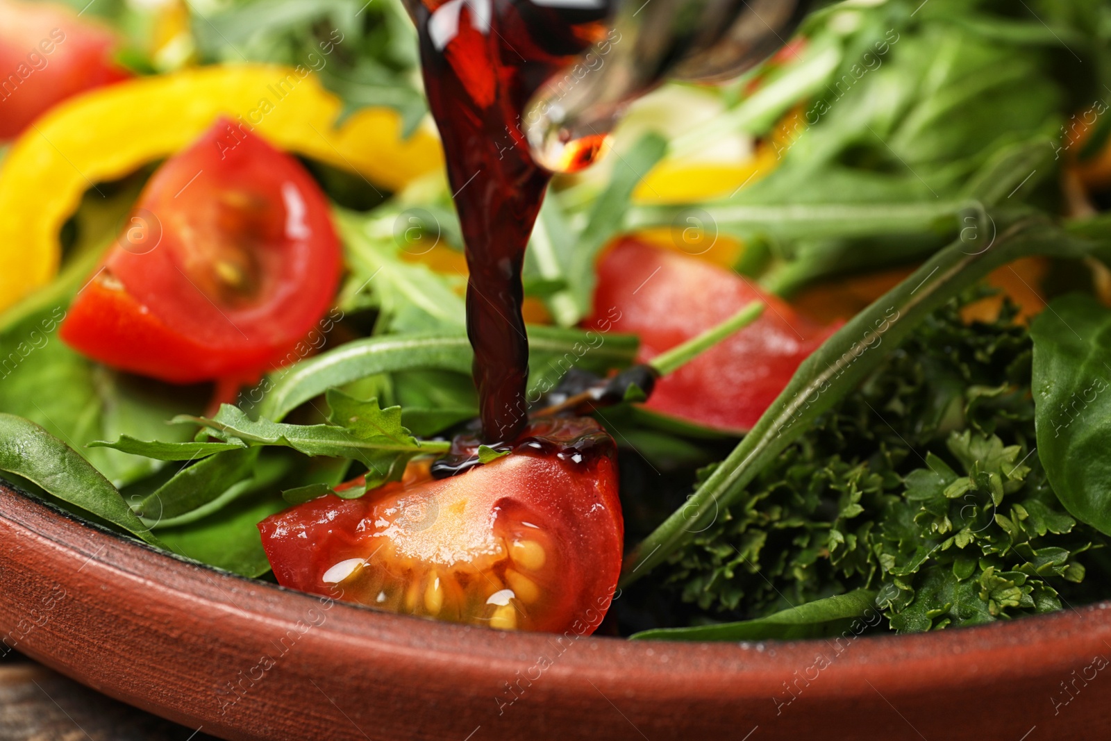 Photo of Pouring balsamic vinegar to fresh vegetable salad on plate, closeup