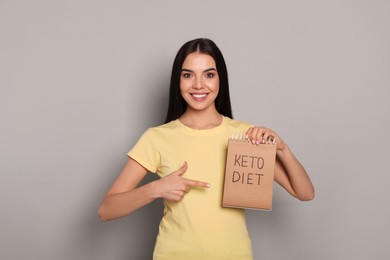 Happy woman holding notebook with words Keto Diet on light grey background