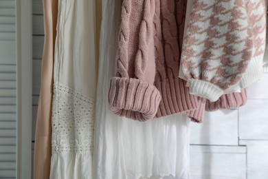 Different stylish clothes near white wall in room, closeup