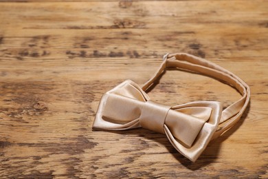 Photo of Stylish beige bow tie on wooden table, closeup. Space for text
