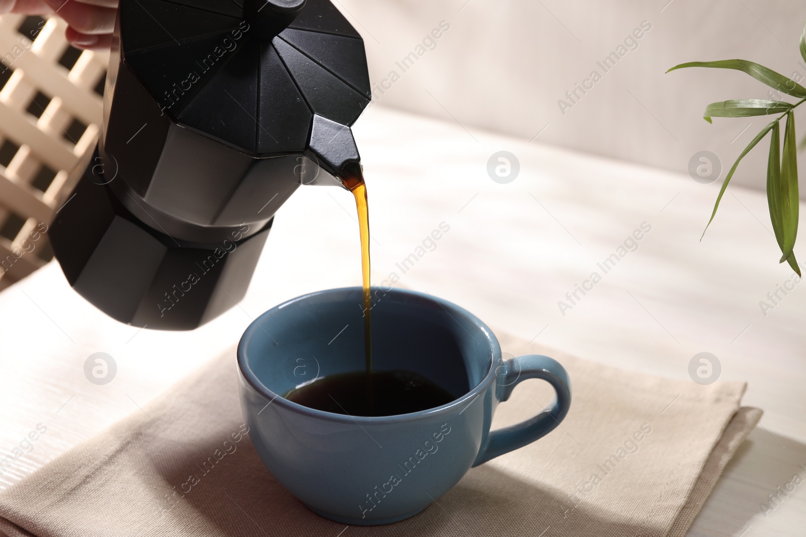 Photo of Pouring aromatic coffee from moka pot into cup at white table, closeup