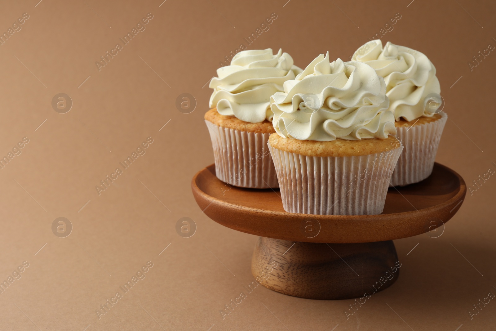 Photo of Tasty vanilla cupcakes with cream on dark beige background, closeup. Space for text