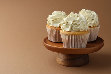 Tasty vanilla cupcakes with cream on dark beige background, closeup. Space for text